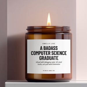 May include: A lit brown glass candle jar with a white label. The label reads "SMELLS LIKE A BADASS COMPUTER SCIENCE GRADUATE" with additional text. The candle is infused with debugging mode, full-stack hustle, and quiet world domination.