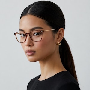 K&ouml;nnte beinhalten: Braune Brille mit quadratischem Rahmen und goldfarbenen B&uuml;geln. Die Brille wird von einer Person mit dunklem, zur&uuml;ckgebundenem Haar getragen. Die Person tr&auml;gt goldene Ohrringe und ein schwarzes Oberteil. Der Hintergrund ist einfarbig hellgrau.
