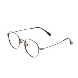 Puede incluir: Un par de gafas redondas con una montura met&aacute;lica fina y oscura. Las gafas cuentan con lentes transparentes, un puente estrecho y varillas delgadas que terminan en puntas de pl&aacute;stico negro. El dise&ntilde;o es sencillo y ligero con almohadillas.