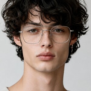 May include: Silver-toned metal eyeglasses featuring a double bridge design and a rectangular frame shape with rounded corners. The glasses have clear lenses and thin, lightweight wire frames that sit across the bridge of the nose.
