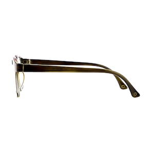 May include: A pair of eyeglasses with a translucent olive green frame viewed from the side. The temple arm features a visible hinge and a small circular metallic detail at the tip. The frame displays the printed text 51 17-140 136 on the inner side.