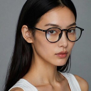 May include: Black-framed, round eyeglasses. The glasses have a classic design with a thin frame and clear lenses. The image is a close-up shot of the glasses, highlighting their shape and style. The background is a solid gray.