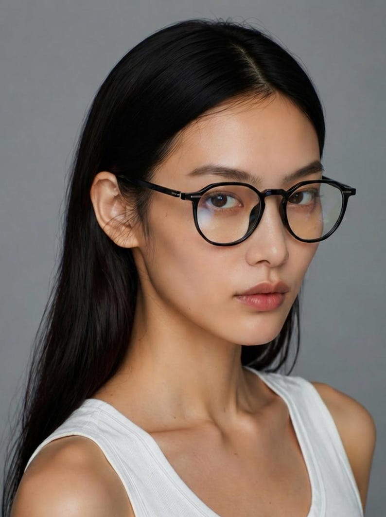 May include: Black-framed, round eyeglasses. The glasses have a classic design with a thin frame and clear lenses. The image is a close-up shot of the glasses, highlighting their shape and style. The background is a solid gray.