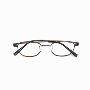 May include: Eyeglasses with a black and brown metal frame. The clear, round lenses are set in a minimalist design. The glasses are suitable for everyday use and have a modern aesthetic.