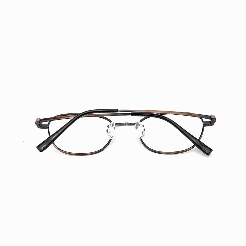 May include: Eyeglasses with a black and brown metal frame. The clear, round lenses are set in a minimalist design. The glasses are suitable for everyday use and have a modern aesthetic.