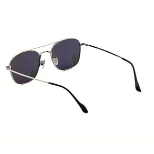 May include: Silver-toned metal sunglasses featuring a double bridge design and dark, tinted lenses. The frames have a rounded rectangular shape with thin, slender temples that end in black plastic tips for a secure fit over the ears.