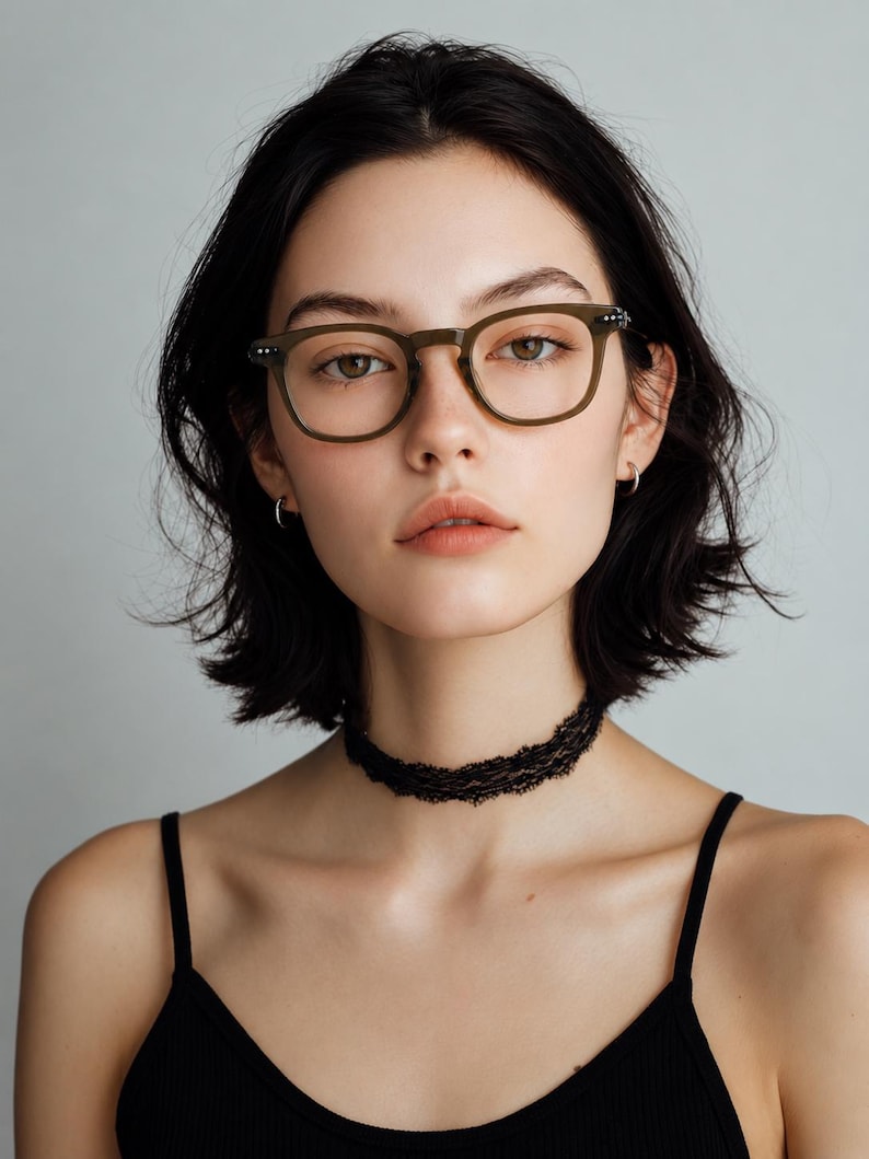 May include: A woman wearing olive green eyeglasses with a square frame and a black lace choker. She is also wearing a black tank top. The background is a solid light gray.