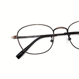 May include: Oval spectacles with a dark brown metal frame. The glasses have a thin frame and black temples. The brand name "Fincher" is printed on the frame. The lenses are clear.