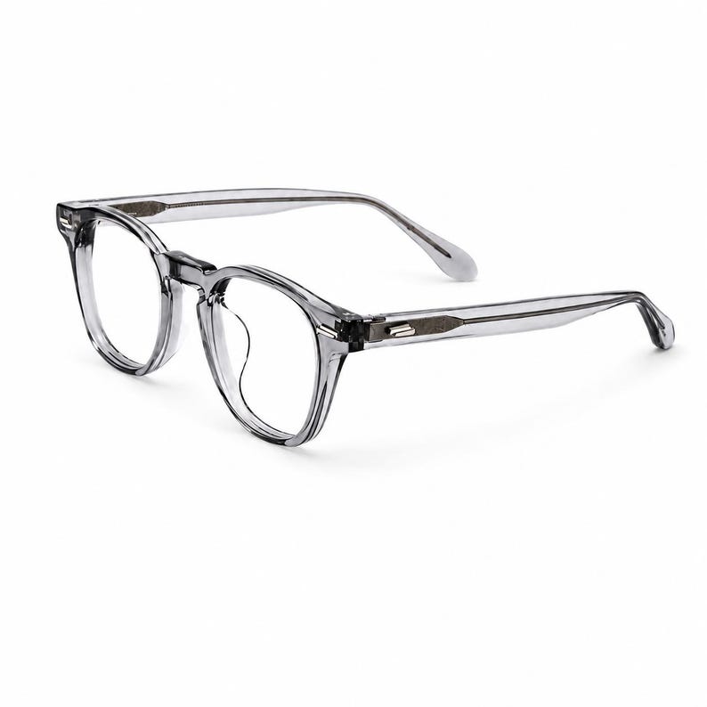 May include: Clear, round-framed eyeglasses with a subtle gray tint. The glasses have a classic design with a keyhole bridge and slender temples. The frames are made of a transparent material, offering a modern and minimalist aesthetic.