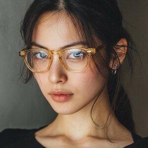 Puede incluir: Retrato de una persona con gafas de montura transparente y tinte marr&oacute;n claro. Las gafas tienen forma cuadrada. La persona lleva una camiseta negra, sobre un fondo gris neutro.