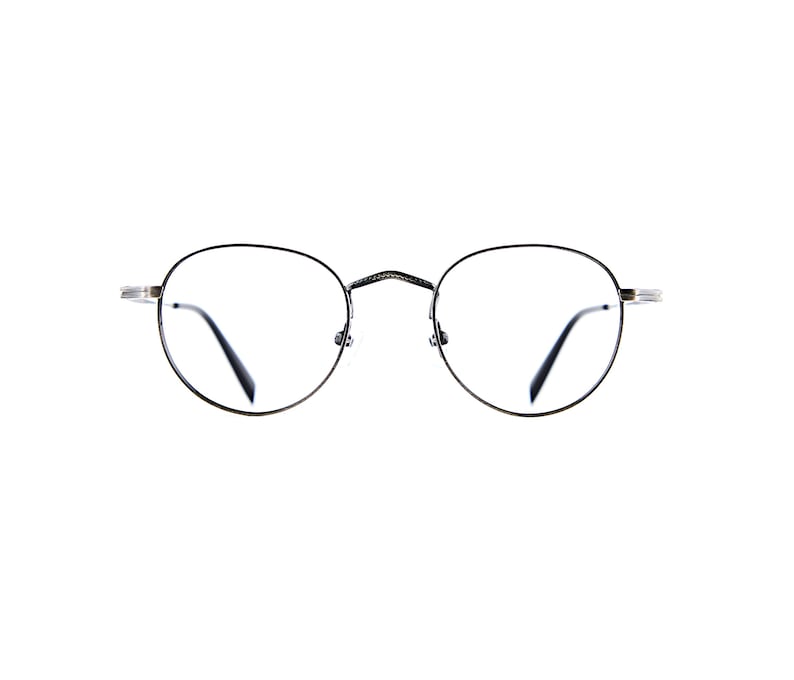 May include: Round eyeglasses with thin, dark metallic frames and clear lenses. The bridge features a textured, cross-hatched pattern, and the temples are slender with a metallic finish. The overall design is simple, featuring circular rims.