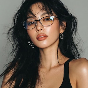 May include: A woman wearing black-framed eyeglasses and hoop earrings. The woman has long, dark hair and is wearing a black tank top. The background is a solid gray.