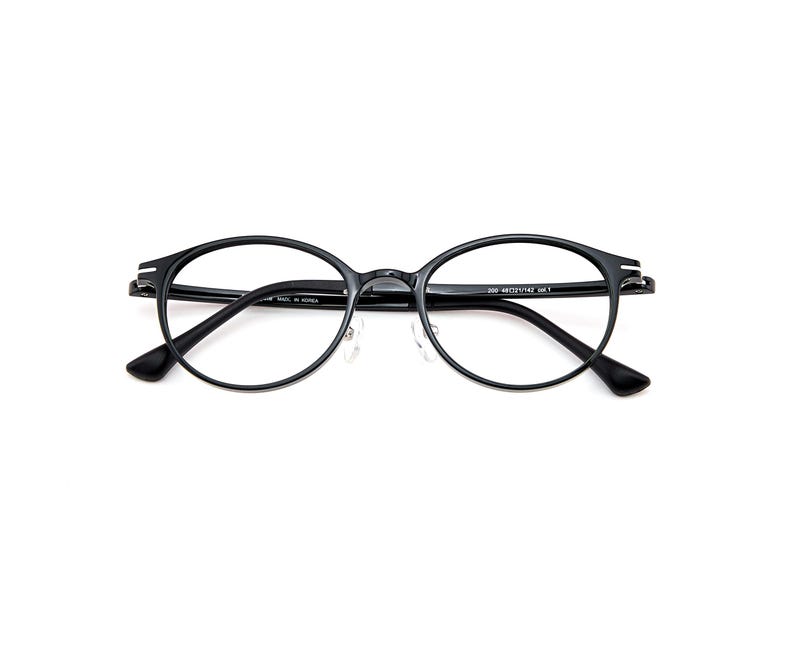 Pode incluir: &Oacute;culos ovais pretos com arma&ccedil;&otilde;es finas e lentes transparentes. A haste interna apresenta texto impresso em branco lendo 200 48 21 142 col.1 e MADE IN KOREA. Os &oacute;culos incluem almofadas nasais ajust&aacute;veis e detalhes prateados nas dobradi&ccedil;as.