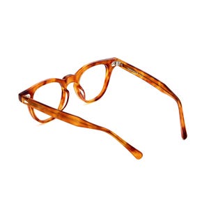 Puede incluir: Gafas con estampado de carey. Las monturas son de color marr&oacute;n c&aacute;lido con vetas marrones m&aacute;s oscuras. Las gafas tienen una forma redonda cl&aacute;sica. La imagen muestra las gafas sobre un fondo blanco.