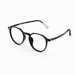May include: Black round-frame eyeglasses with clear lenses. The glasses have a modern design with a matte finish and gold-colored accents on the temples. The frame is made of a durable material, and the lenses are clear and ready for prescription.