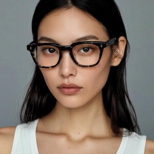 Könnte beinhalten: Quadratische Brille mit Schildpattmuster. Die Brille hat eine dunkelbraune und schwarze Farbgebung mit kleinen rautenförmigen Akzenten an den Bügeln. Die Gläser sind klar, und der Rahmen ist dick und stabil.