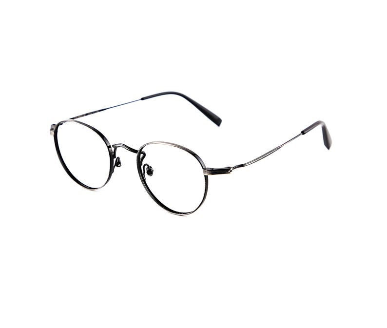 May include: A pair of round eyeglasses with a thin, dark metallic frame. The glasses feature clear lenses, a slender bridge, and thin, straight temples with dark tips, providing a lightweight and simple structure for everyday vision correction.
