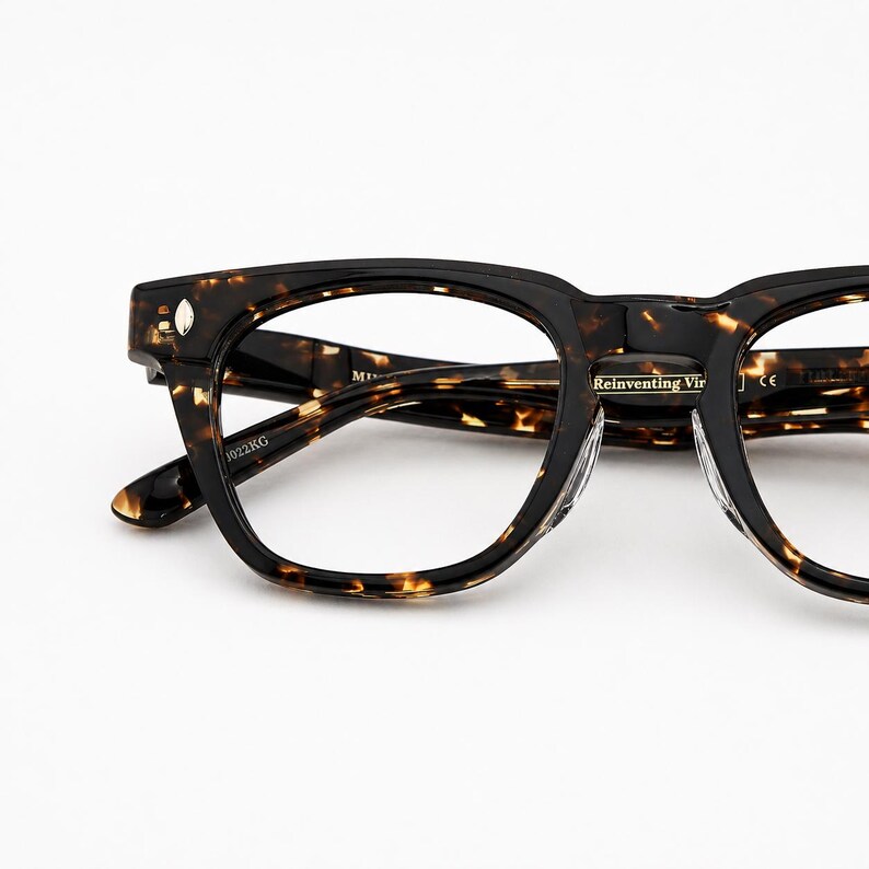 Puede incluir: Primer plano de gafas con un patr&oacute;n carey marr&oacute;n oscuro. Las monturas tienen forma cuadrada con bordes redondeados. El texto "Reinventing Vir" es visible en el puente. Las patillas son de color marr&oacute;n oscuro liso.