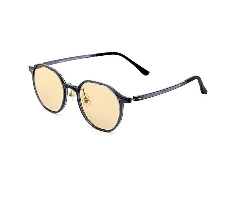 May include: Round-framed glasses featuring translucent dark gray frames and light yellow-tinted lenses. The eyewear includes thin, dark gray temples with black tips and gold-toned nose pads, providing a clear view of the front and side profile.