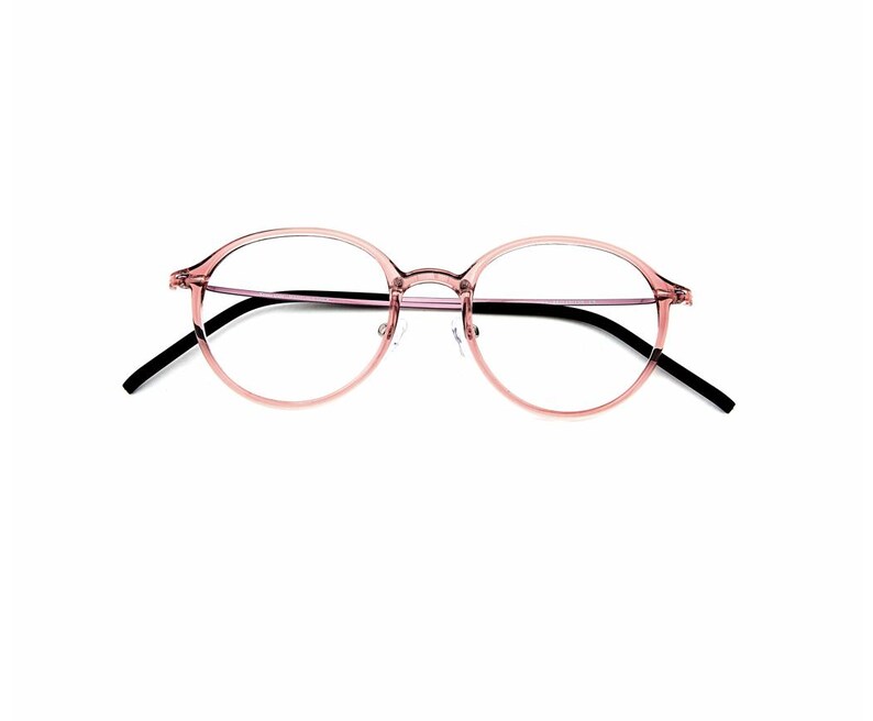May include: Round eyeglasses featuring a translucent, light pink plastic frame. The thin temples are black, providing a contrast to the soft-colored front. These glasses have a bridge and clear lenses, designed with a simple, functional structure.