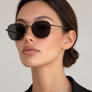 May include: Black sunglasses featuring a thin metal frame with a double bridge design and dark tinted lenses. The eyewear has a classic navigator shape with slender temples and adjustable nose pads, providing a sleek and functional look.