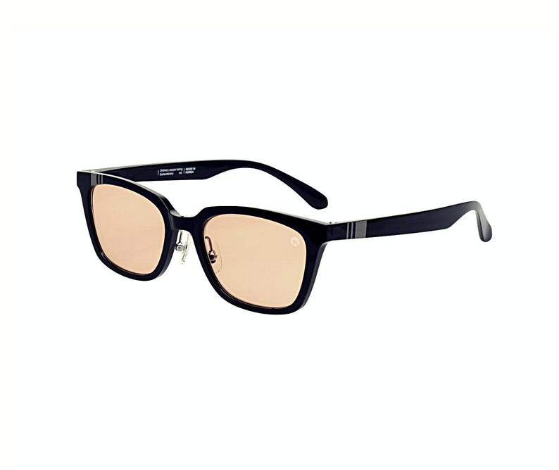 May include: Black rectangular sunglasses with light brown lenses. The frames have a subtle silver stripe on the temples and a small logo on the side. The sunglasses are set against a white background.