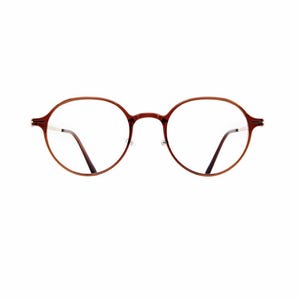 May include: Round eyeglasses featuring a glossy, dark reddish-brown acetate frame with a thin bridge and slim, metallic-toned temples. The lenses are clear and circular, held within a smooth, polished rim that connects to the arms at the outer edges.