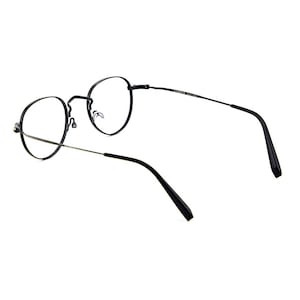 May include: Black eyeglasses with thin, round metal frames and clear lenses. The glasses feature slender temples with black plastic tips and a bridge connecting the two circular rims. The design is simple, with a focus on the thin metal construction.