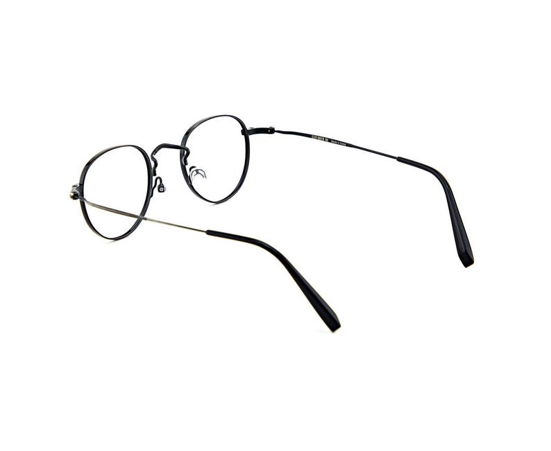 May include: Black eyeglasses with thin, round metal frames and clear lenses. The glasses feature slender temples with black plastic tips and a bridge connecting the two circular rims. The design is simple, with a focus on the thin metal construction.
