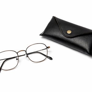 May include: Eyeglasses with a thin, gold-coloured metal frame and black arms, beside a black leather glasses case with a gold-coloured button clasp. The glasses have clear lenses.