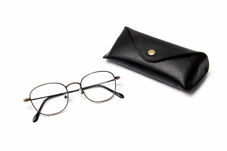 May include: Eyeglasses with a thin, gold-coloured metal frame and black arms, beside a black leather glasses case with a gold-coloured button clasp. The glasses have clear lenses.