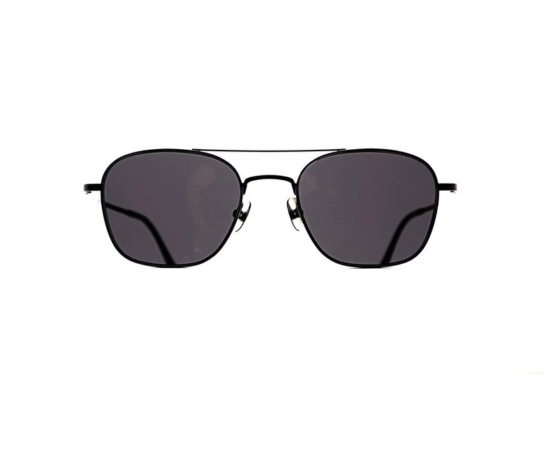 May include: Black sunglasses featuring a thin metal frame with a double bridge design and dark, tinted lenses. The rounded square frames are connected by a slender top bar, creating a sleek and uniform appearance with dark temple arms visible.