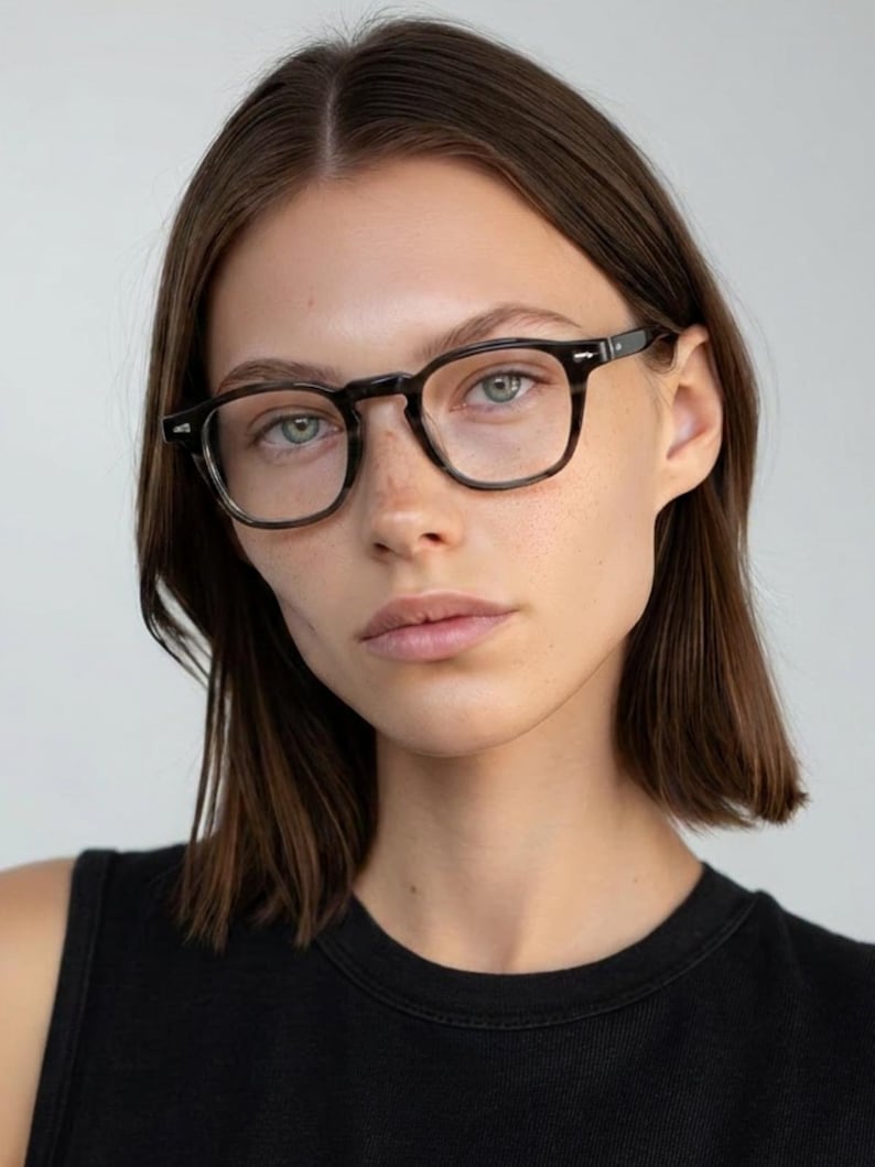 May include: Dark-framed eyeglasses with a square shape. The frames are a dark, mottled color. The model is wearing a black tank top. The background is a plain, light color.