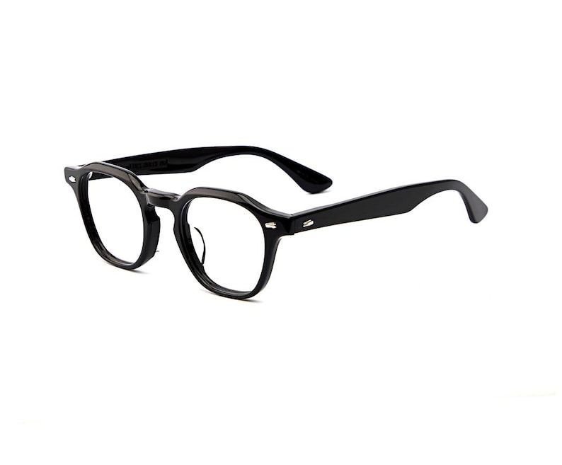 May include: Black eyeglasses with a thick, glossy acetate frame featuring a rounded, slightly angular shape. The glasses have clear lenses, sturdy temples, and small silver-toned metal rivets on the front corners of the frame near the hinges.