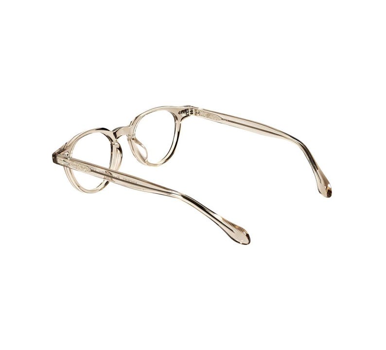 May include: Clear, round-framed eyeglasses with a light brown tint. The glasses have a classic design with thin temples and a keyhole bridge. The frames are made of a translucent material, and the lenses are clear.