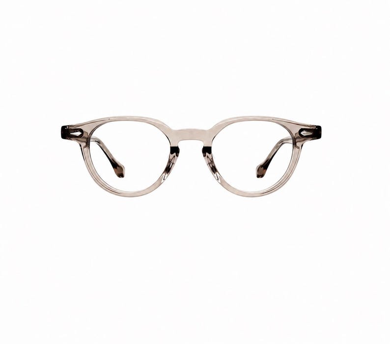 May include: Clear, round-framed eyeglasses with a light gray tint. The frames have a subtle, translucent appearance, and the temples are a darker shade of gray. The lenses are clear, and the overall design is minimalist and modern.