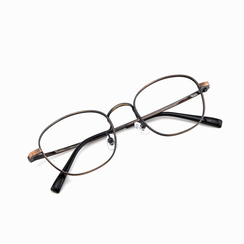 May include: Oval eyeglasses with a bronze frame and black arms. The clear lenses are set in a vintage-style frame. The brand name "Freder" is visible on the frame. The glasses are suitable for everyday use.