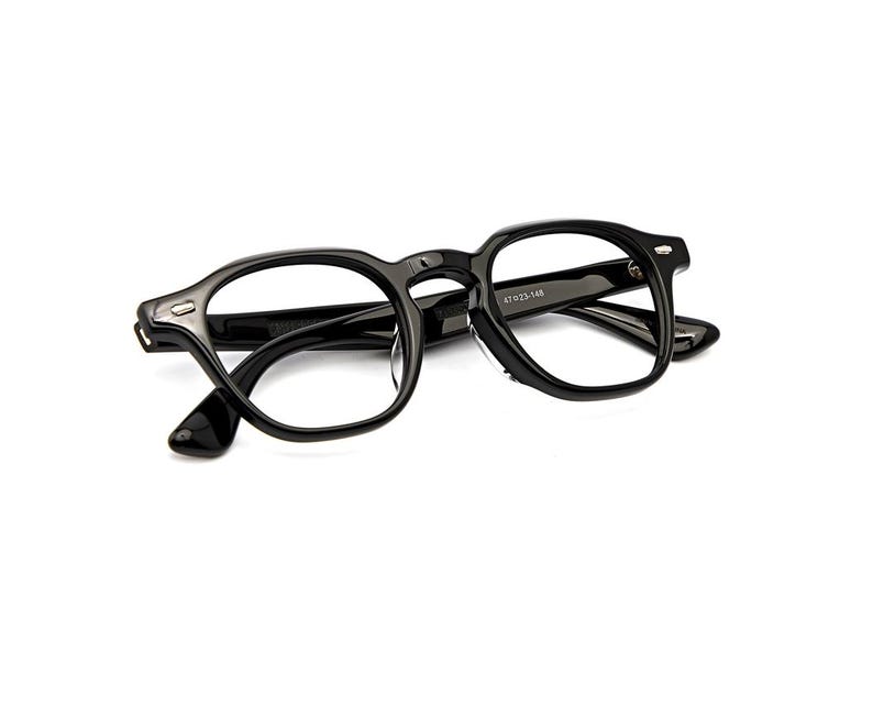 May include: Glossy black eyeglasses featuring a thick, rounded rectangular frame with silver-toned metal rivets at the hinges. The inner temple arm displays the printed text 47 23-148, indicating the frame measurements in millimeters.