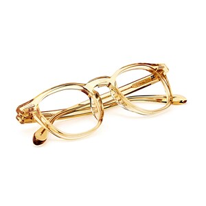 Puede incluir: Un par de gafas transparentes de color marr&oacute;n claro con montura rectangular redondeada. Las gafas tienen un dise&ntilde;o cl&aacute;sico con puente de cerradura y est&aacute;n sobre un fondo blanco.