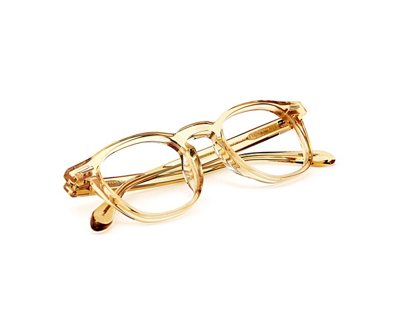 Puede incluir: Un par de gafas transparentes de color marr&oacute;n claro con montura rectangular redondeada. Las gafas tienen un dise&ntilde;o cl&aacute;sico con puente de cerradura y est&aacute;n sobre un fondo blanco.