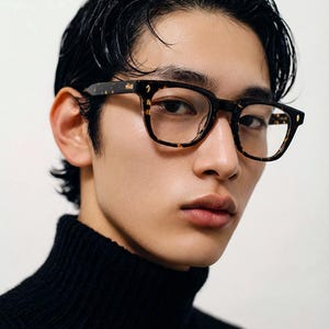 Puede incluir: Gafas de montura cuadrada con estampado de carey. Las gafas tienen un dise&ntilde;o marr&oacute;n oscuro y beige. La persona de la imagen lleva un jersey de cuello alto negro. El fondo es blanco liso.