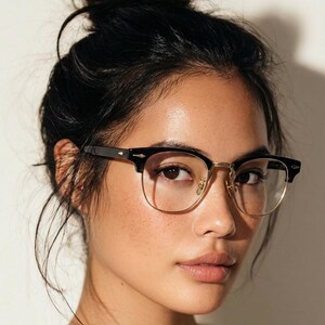 May include: Browline glasses featuring a black upper frame and thin gold-tone metal rims. The design includes small gold-tone metal rivets on the outer corners of the black brow pieces and adjustable nose pads attached to the bridge of the frame.