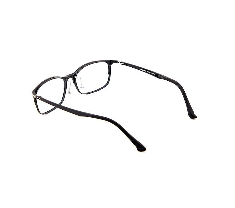 Puede incluir: Gafas rectangulares negras con lentes transparentes. Las monturas son de color negro mate con detalles plateados en las bisagras y las patillas. Las gafas est&aacute;n sobre un fondo blanco.