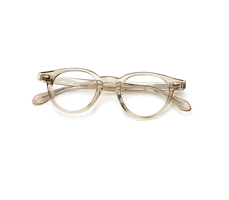May include: A pair of clear, round-framed eyeglasses. The frames are a light, translucent brown color. The glasses have a classic, vintage design, with a keyhole bridge and subtle detailing on the temples.
