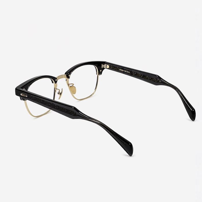 May include: Black and gold browline glasses featuring a semi-rimless frame design with clear lenses. The temples are black with an intricate engraved pattern along the sides. The inner temple is printed with the text 48-20-145 Col.1.