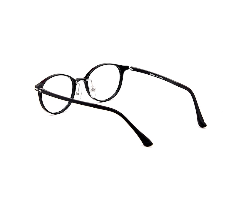 Pode incluir: &Oacute;culos de arma&ccedil;&atilde;o redonda preta com lentes transparentes e hastes finas. A arma&ccedil;&atilde;o apresenta uma ponte com almofadas nasais ajust&aacute;veis e detalhes em metal prateado nas dobradi&ccedil;as. A haste interna cont&eacute;m texto impresso sobre a origem.