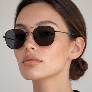 May include: A pair of sunglasses featuring a thin, dark metal frame with a double bridge design and dark, solid-colored lenses. The eyewear has slender temples and adjustable nose pads, providing a sleek and functional look for eye protection.