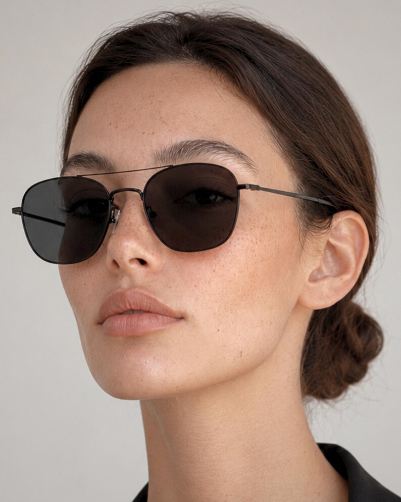 May include: A pair of sunglasses featuring a thin, dark metal frame with a double bridge design and dark, solid-colored lenses. The eyewear has slender temples and adjustable nose pads, providing a sleek and functional look for eye protection.