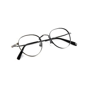 May include: A pair of round eyeglasses with a thin, dark metallic frame. The glasses feature clear lenses, a delicate bridge with a textured pattern, and black temple tips. The frame is constructed from a slender metal material with a dark finish.