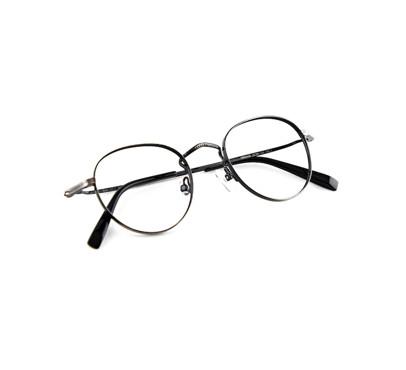May include: A pair of round eyeglasses with a thin, dark metallic frame. The glasses feature clear lenses, a delicate bridge with a textured pattern, and black temple tips. The frame is constructed from a slender metal material with a dark finish.